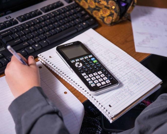 A calculator sits atop a spiral-bound notebook on a student's desk.